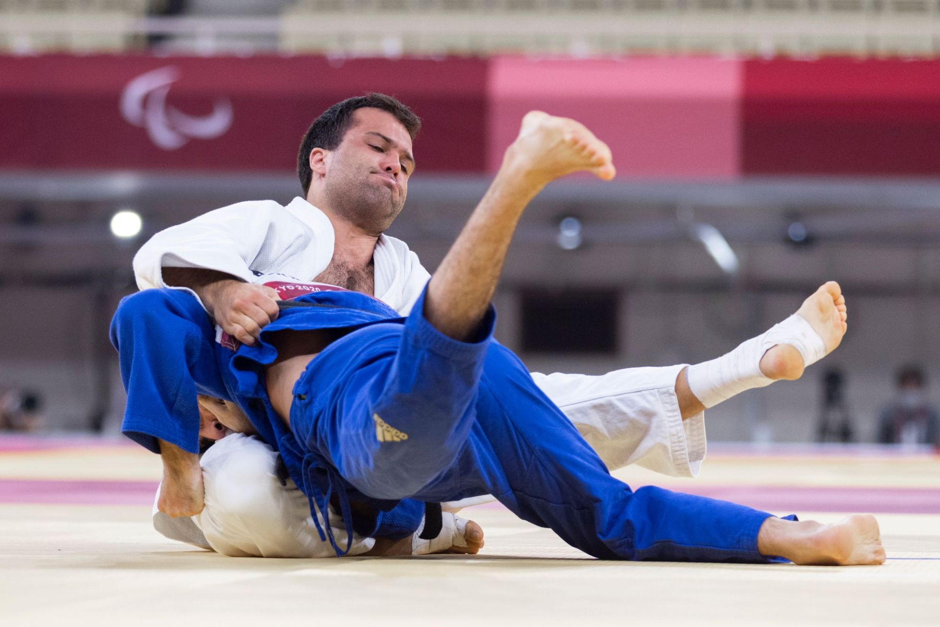 A judoka in a white judogi driving an opponent in blue to the mat during a tournament throw
